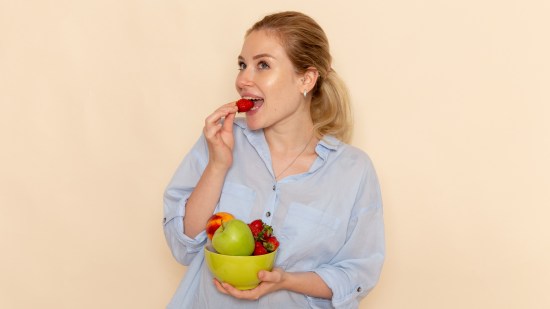 front-view-young-beautiful-female-shirt-holding-plate-with-fruits-eating-strawberry-cream-wall-fruit-ripe-model-woman-pose