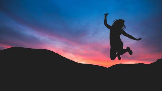 silueta de mujer saltando feliz entre montañas en una puesta de sol