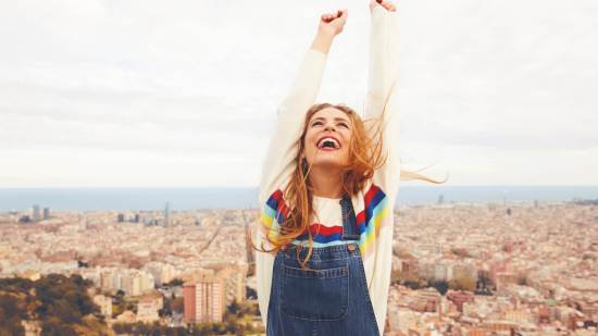 mujer feliz levantando los brazos con una ciudad al fondo
