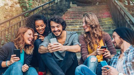 grupo de cinco amigos mirando sus telefonos moviles