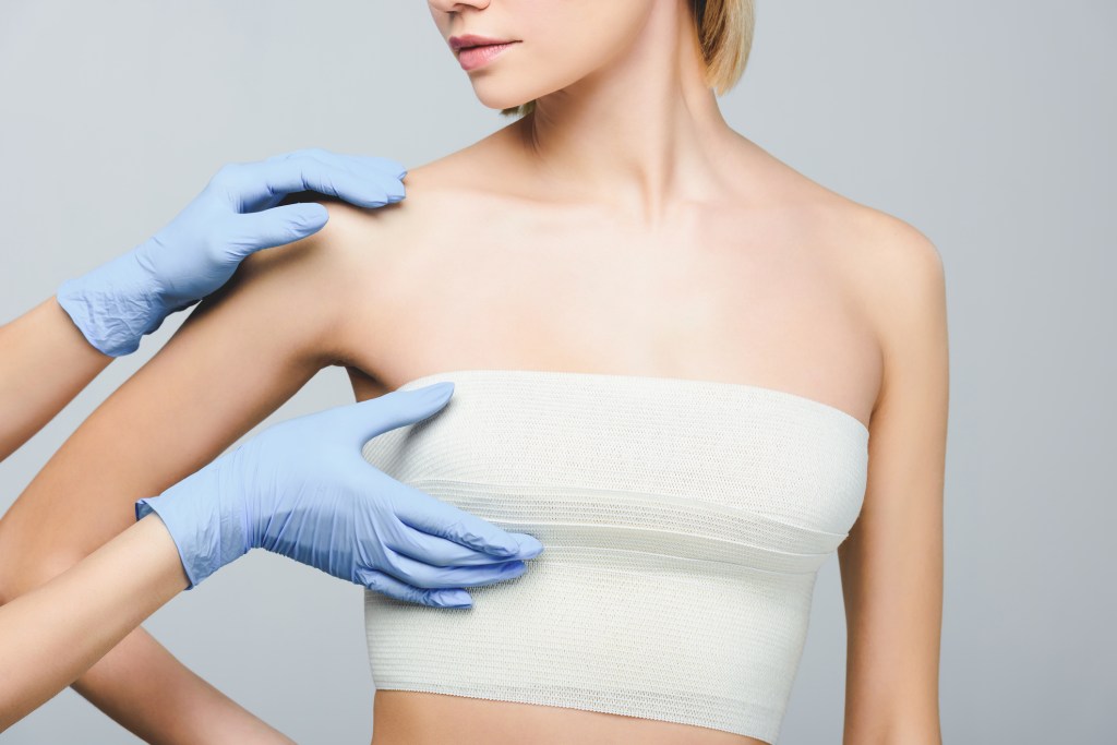 Cirujano plástico en guantes de látex comprobando el pecho femenino - iStock