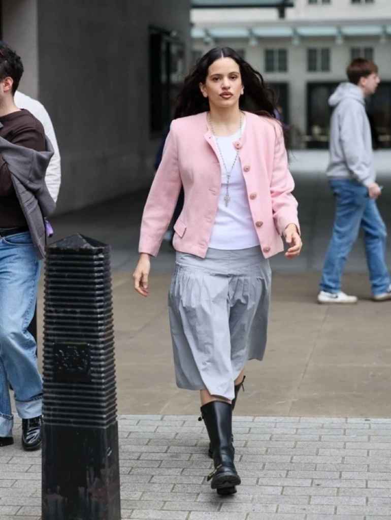 La cantante Rosalía paseando por Londres con un look con chaqueta rosa, rosario y botas moteras