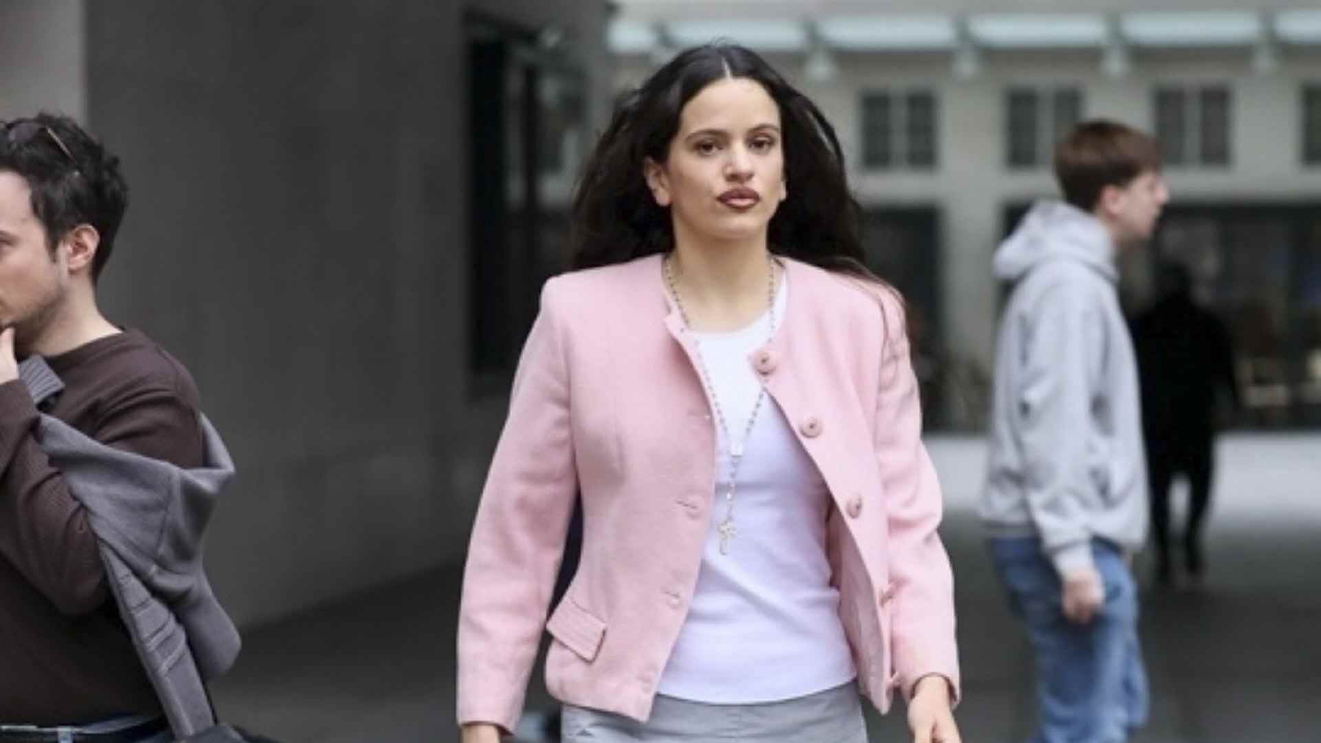 La cantante Rosalía paseando por Londres con un look con chaqueta rosa, rosario y botas moteras